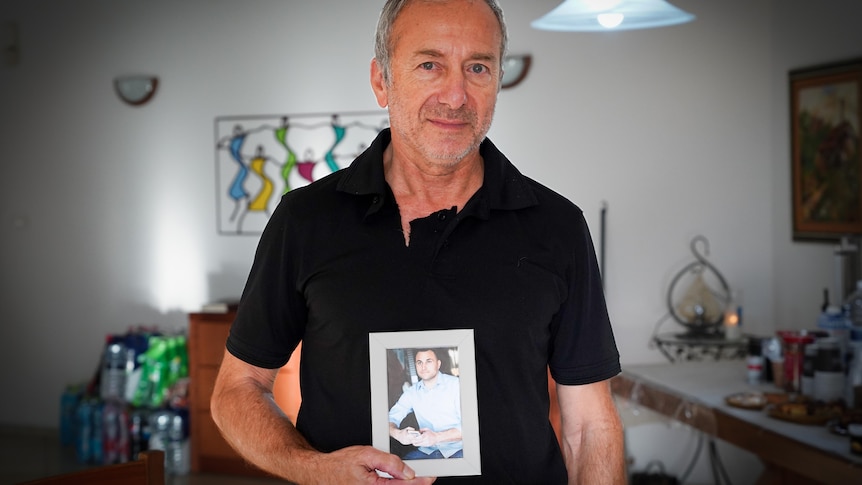 A man in a black shirt holds a framed photo of a young man