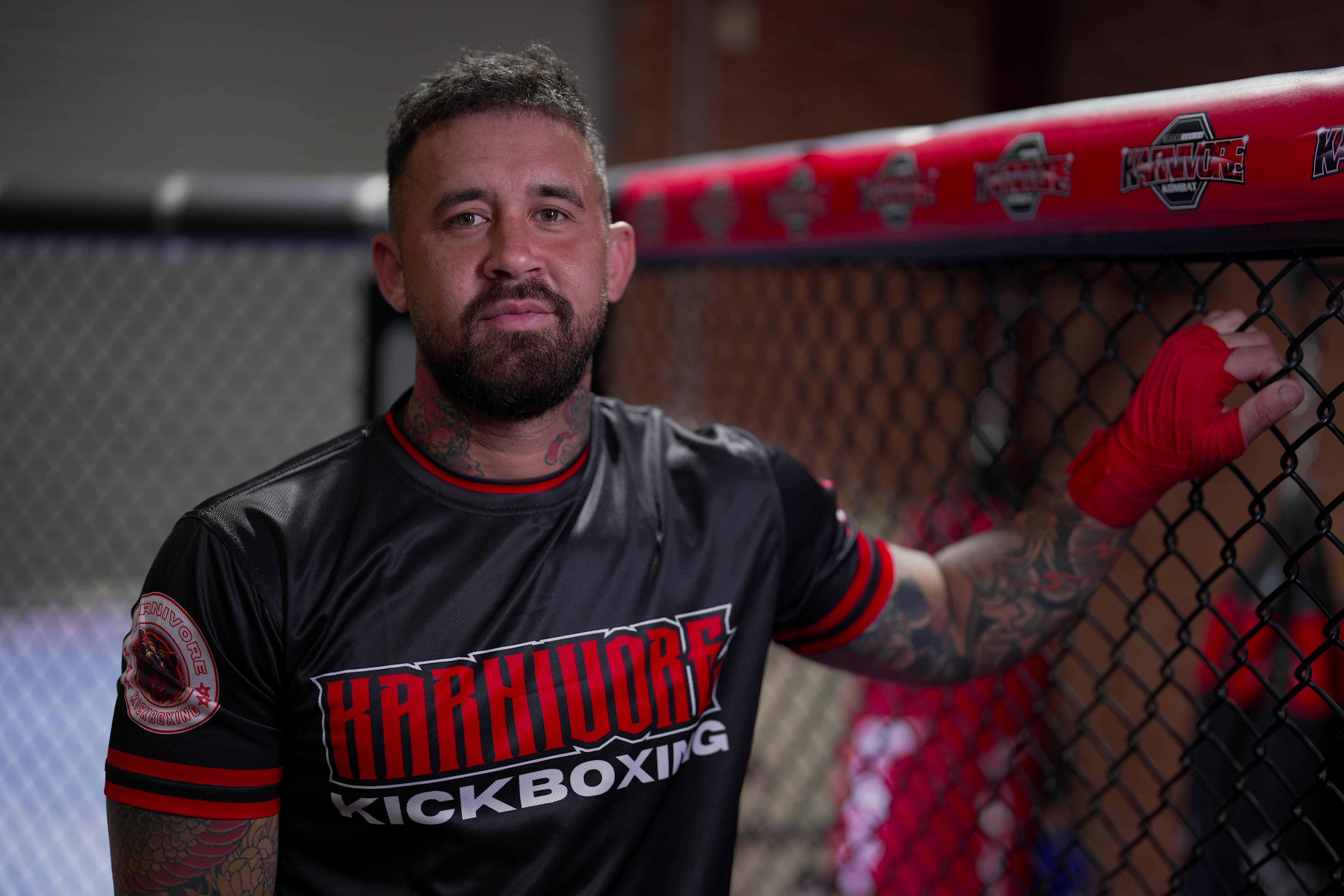 A man stands in a gym wearing a shirt that says 'kickboxing' on it.