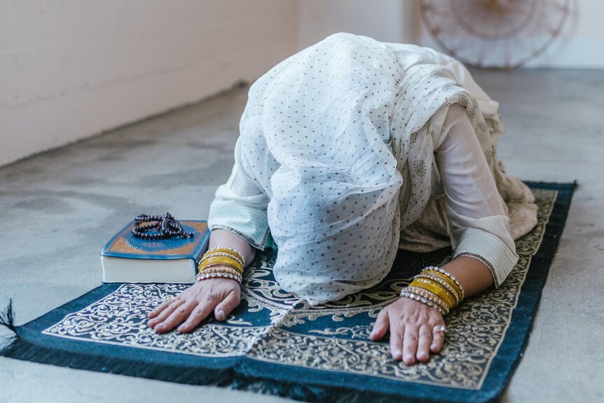 Muslim woman wearing headscarf in prayer position on prayer mat.