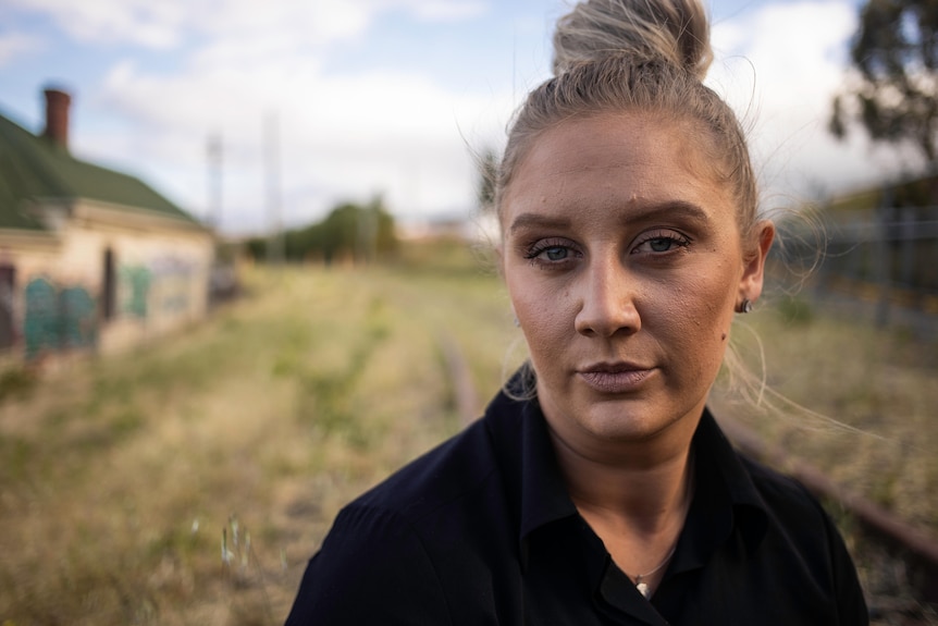 Woman with her hair up in a bun wearing a jacket, standing outside.