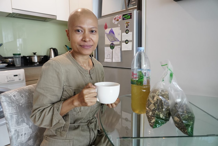 A woman sits at a table with a tea cup and bags of dried marijuana