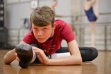 Ballet student Presley Tanner stretches his leg while seated on the ground