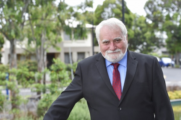 Barry Calvert in a black blazer, red tie and blue shirt with a beard