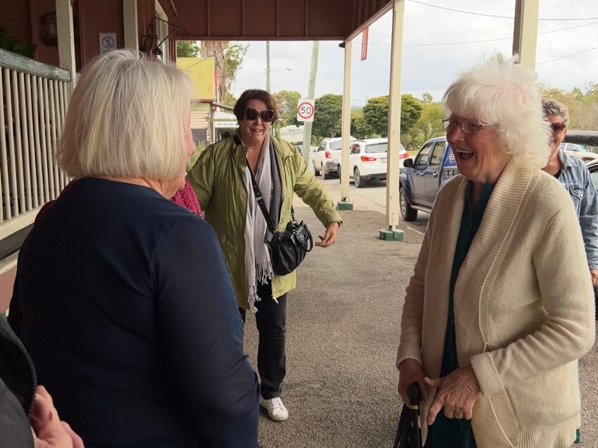 Two elderly women laugh having a conversation, while two others look on.