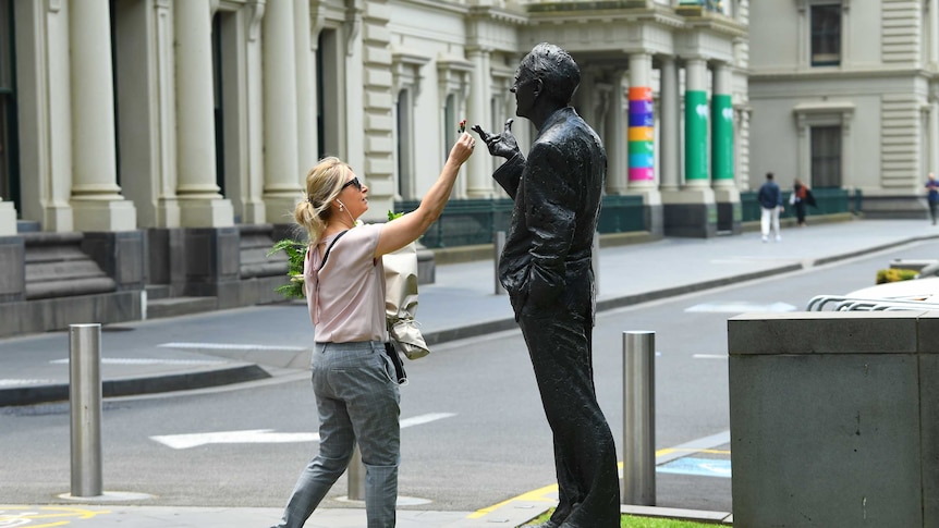 A woman puts a flower on a statue of John Cain.