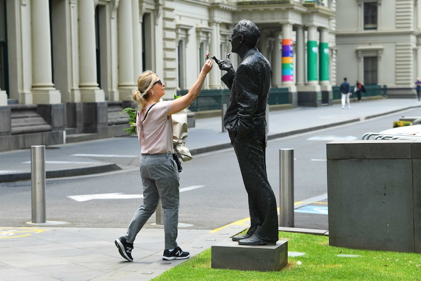 A woman puts a flower on a statue of John Cain.