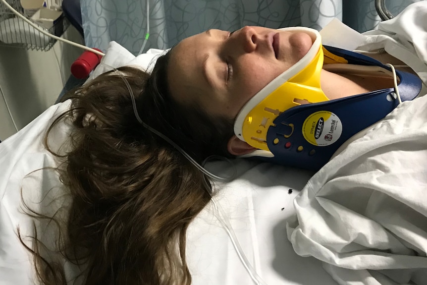 A woman laying on a hospital bed, her head supported by a neck brace