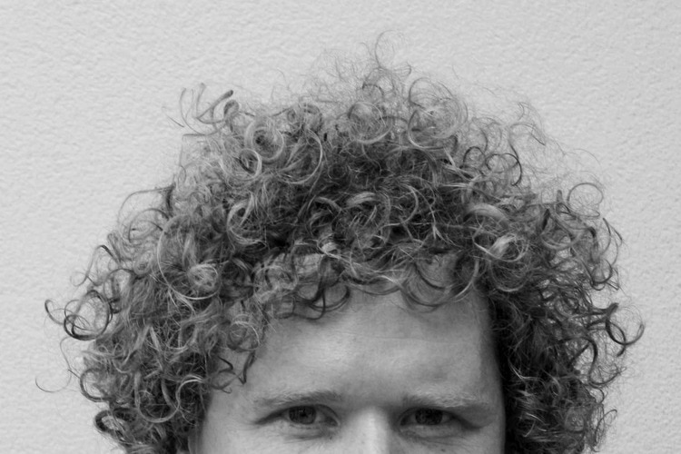 A black and white headshot of a curly-haired composer