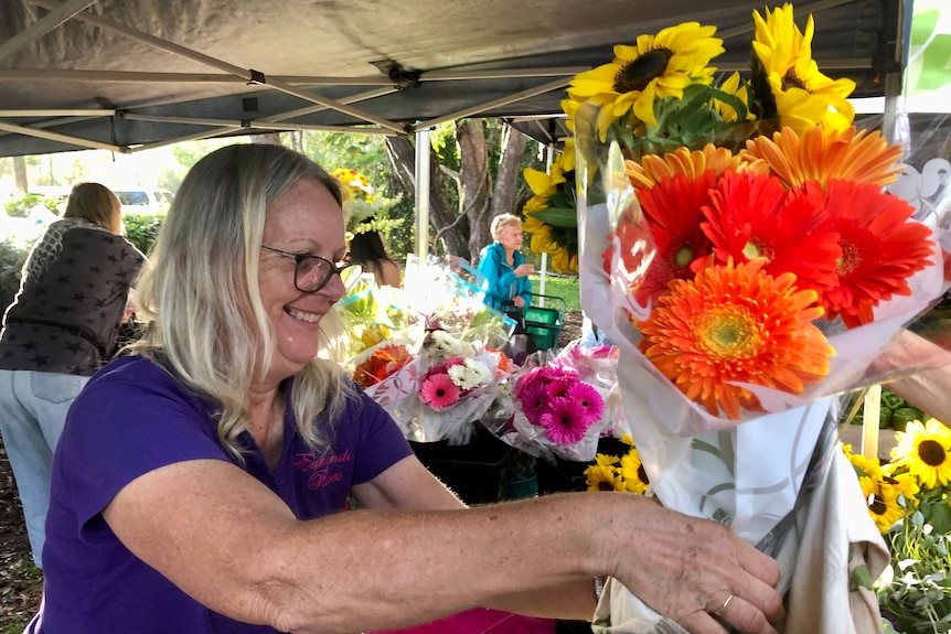 A woman handing over two bunches of flowers, sunflowers and gerberas.