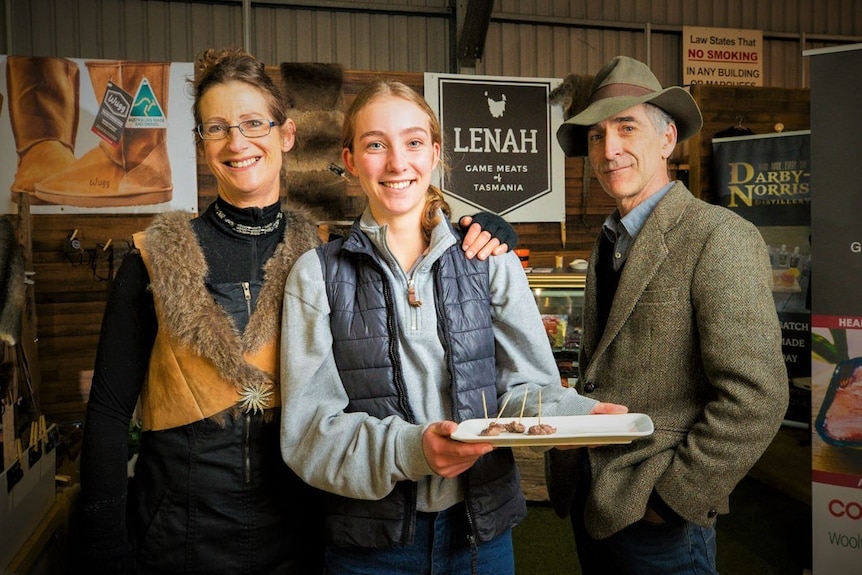 A man, a woman and a teenage girl standing in front of a promotional stall at an event.