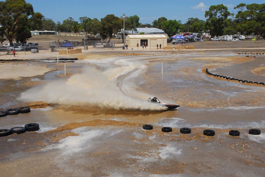 A V8 jet boat goes around a wet, dirt track.