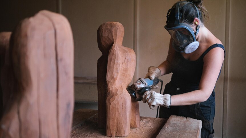 The artist uses a tool to carve a piece of warm red wood into a sculptural form.