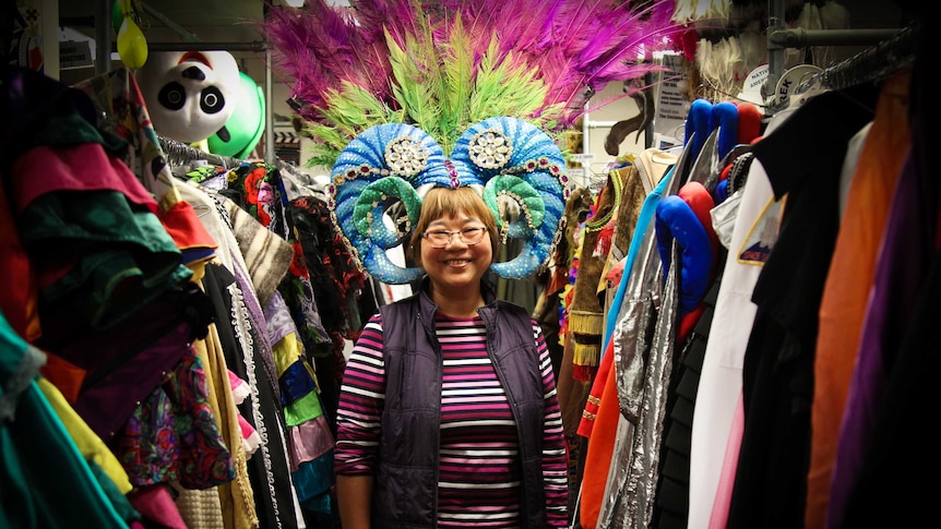 Kitty Hoh dressed in a Priscilla wig, standing in a row of costumes.