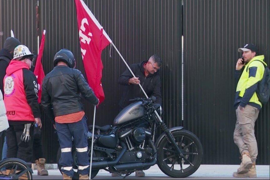 A man puts a CFMEU flag on a motorbike. 
