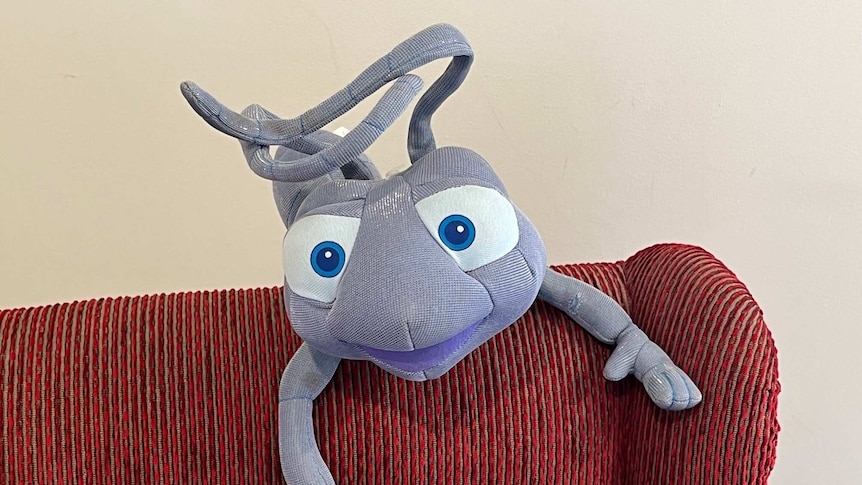 A soft toy of the Disney character Flik from 'A Bug's Life' perched on a chair.