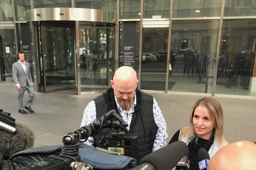 A bald man with a beard and a woman with blonde hair speak to media outside court.