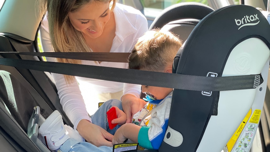 A woman buckles a seat belt in car seat with son inside.