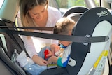A woman buckles a seat belt in car seat with son inside.