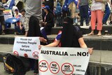 Two people wear niqabs while holding anti-refugee and anti-Islamic signs.