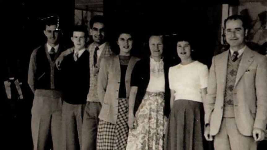 A black and white photo showing a group of men and women standing in front of a store with the Assef's sign.