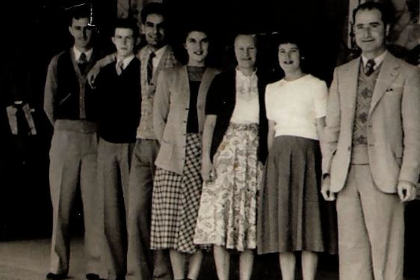 A black and white photo showing a group of men and women standing in front of a store with the Assef's sign.