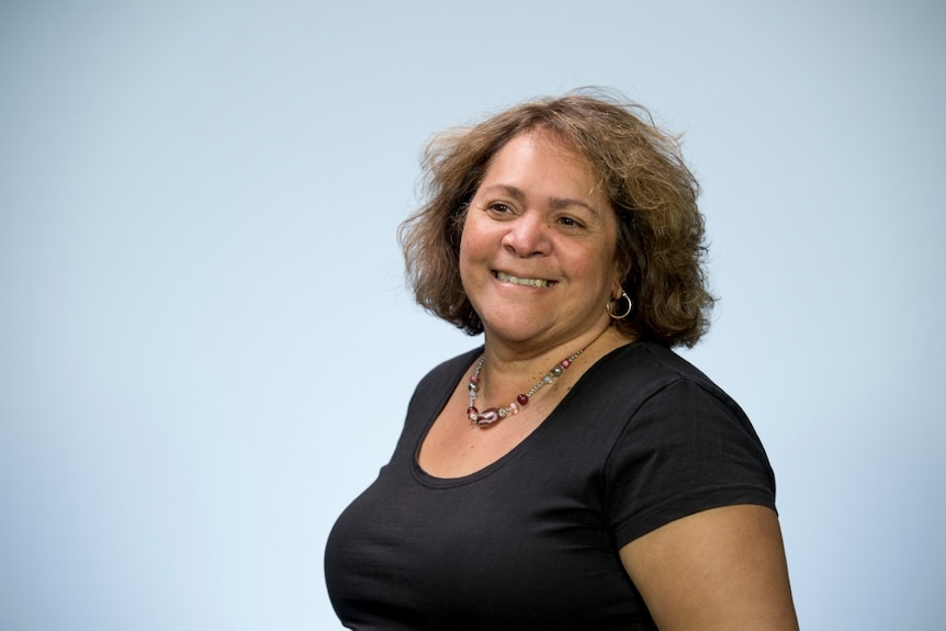 A headshot of a woman, in the right-hand-side of the frame, smiling and wearing a black shirt.