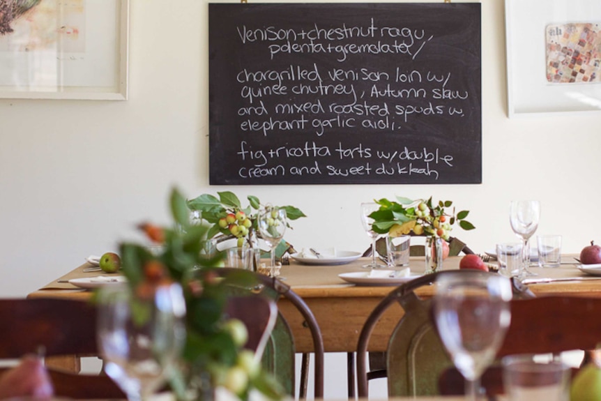 A table setting with a blackboard in the background with a menu including venison dishes