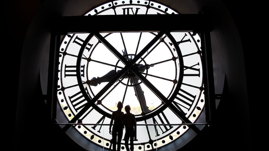 A photo of a clock taken from inside the Orsay museum in Paris with two people standing in front of it.