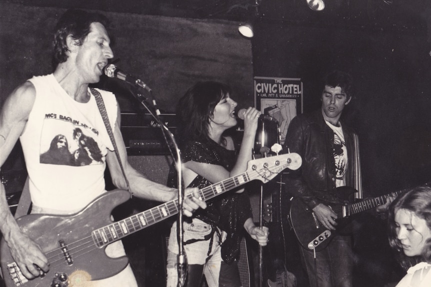 A black and white photo of Ron Blake playing guitar and singing with a band on stage