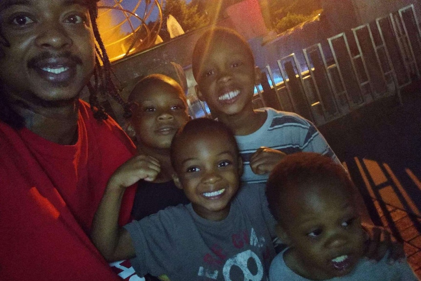 A man in a red shirt smiling with four young boys.