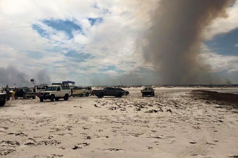 Cars on the beach at Wedge Point, while the bushfire blazes around Wedge Island, north of Lancelin in WA