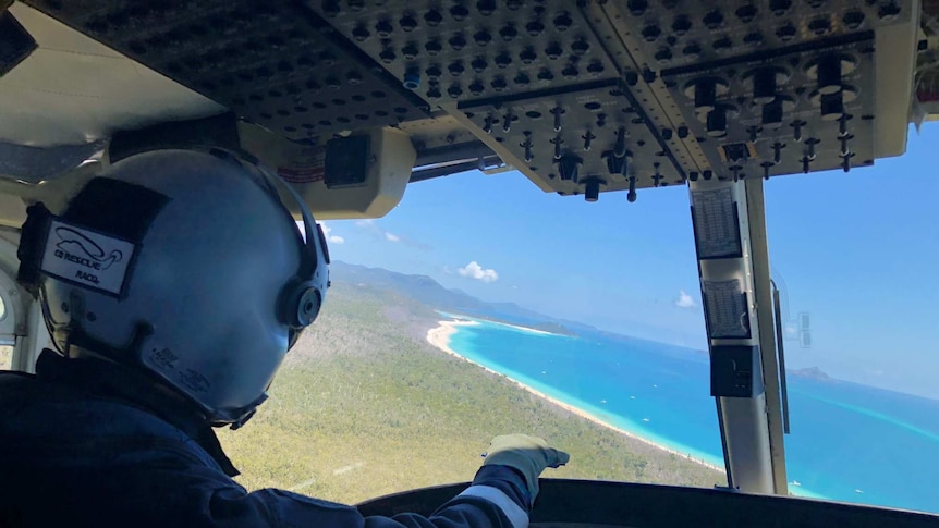 The pilot on board the helicopter points to Cid Harbour, the blue ocean surrounded by a white sand beach.