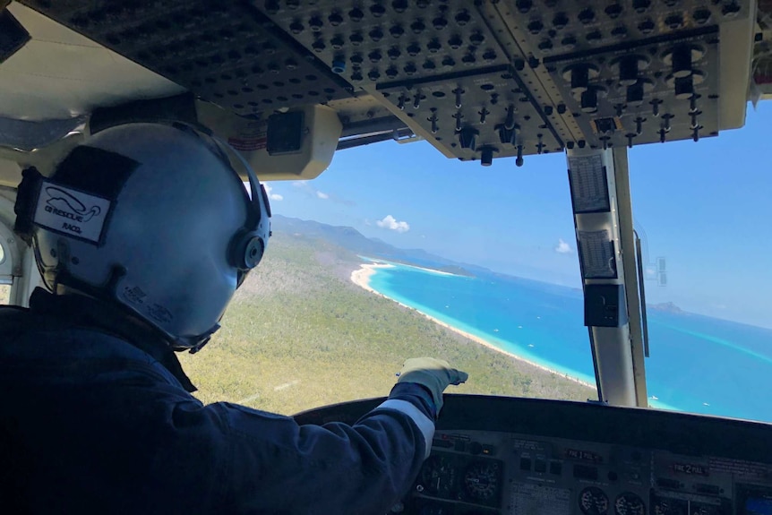 The pilot on board the helicopter points to Cid Harbour, the blue ocean surrounded by a white sand beach.