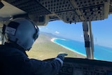 The pilot on board the helicopter points to Cid Harbour, the blue ocean surrounded by a white sand beach.