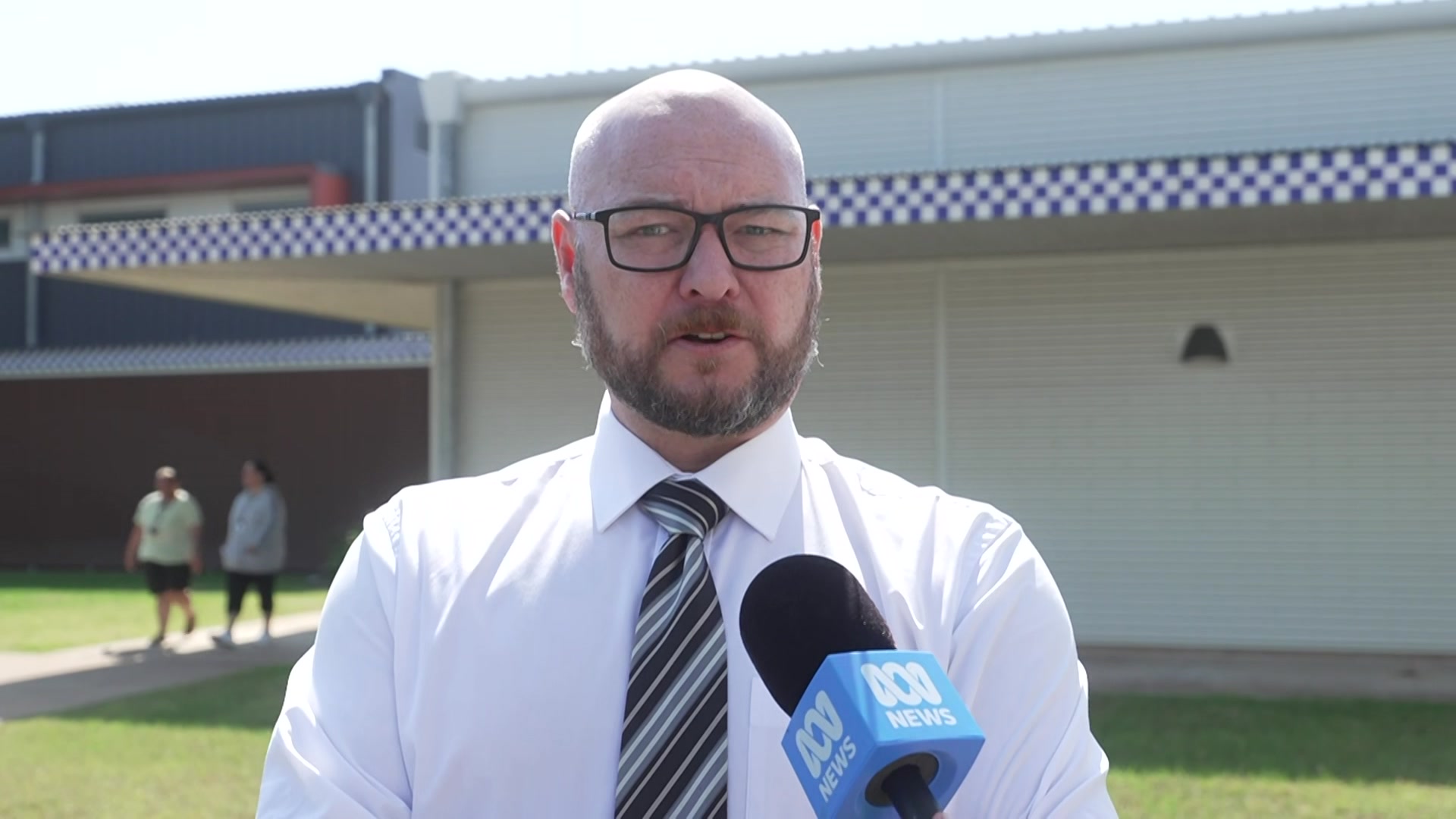 A white man standing in front of police station in a white shirt and striped tie with serious expression.