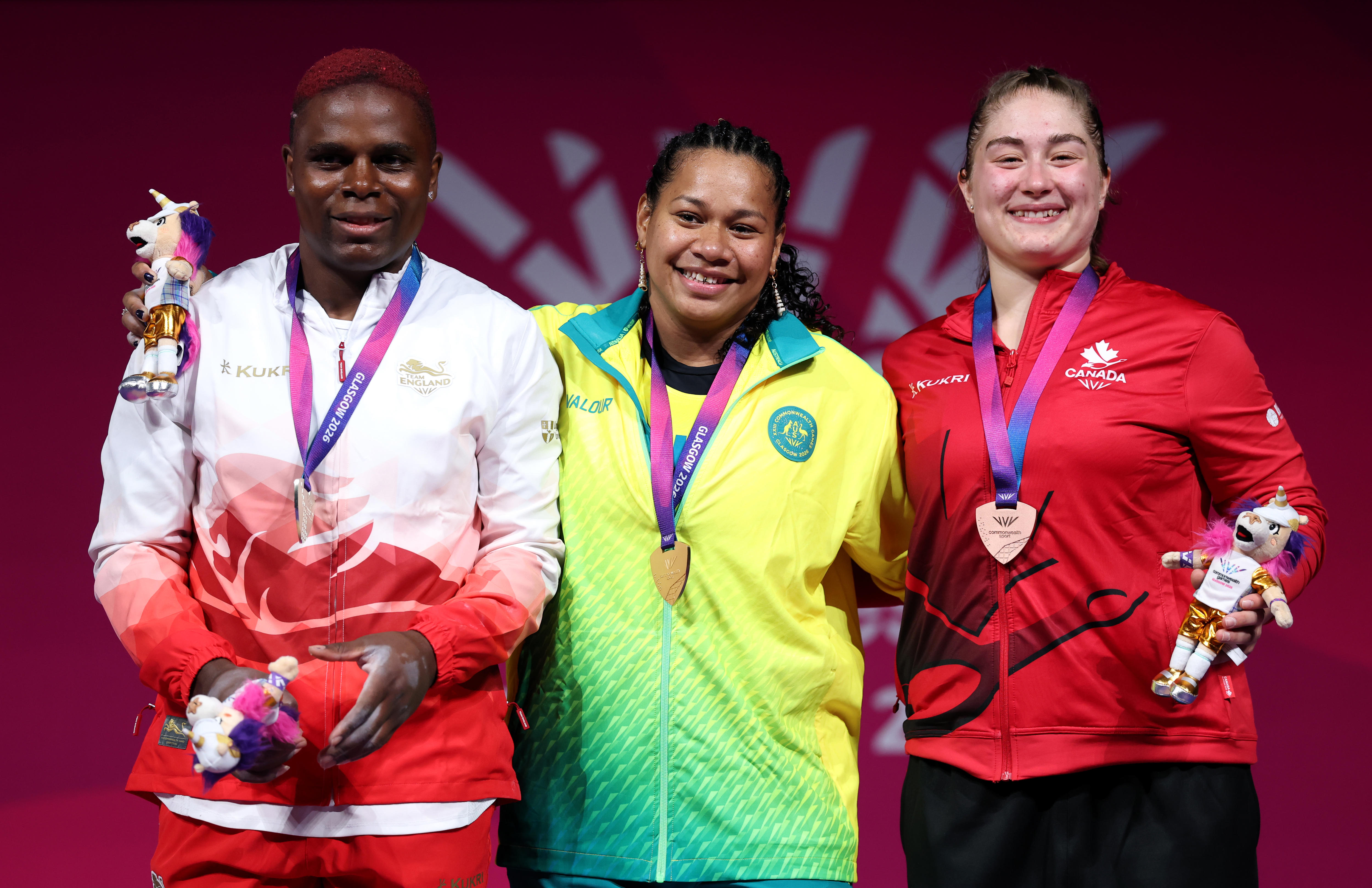 Three women stand on a podium and show off their medals.