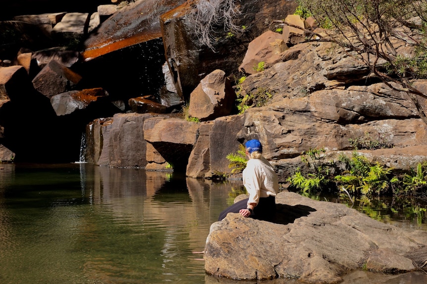 A woman sitting on a rock, water in the rock pool, water falling down the rocks.
