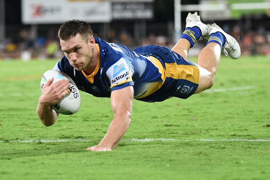 A Parramatta Eels NRL player holds the ball with his right arm as he dives to score a try against Brisbane.