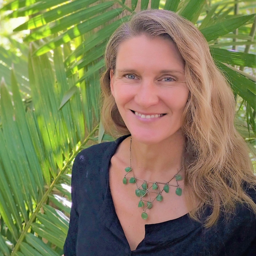 woman standing in front of green plants, smiling