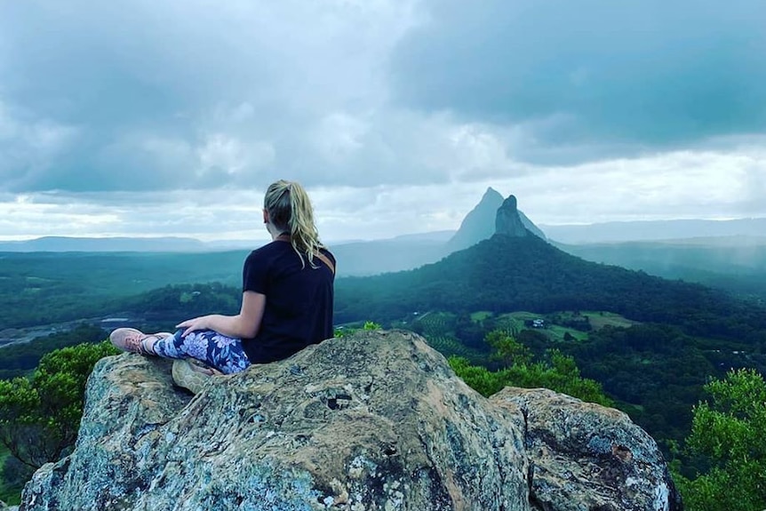 The back of a girl, sitting on the summit, looking out over the Glass House Mountains.