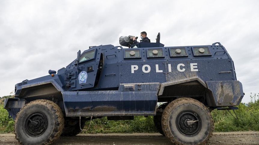 An officer points a noise cannon atop an armoured police vehicle