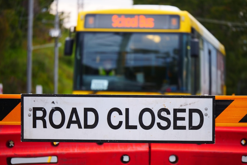 A bus behind a sign that says "road closed".