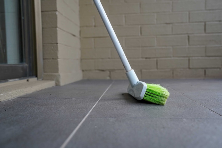 A broom rests against a brick wall on the balcony of an apartment.