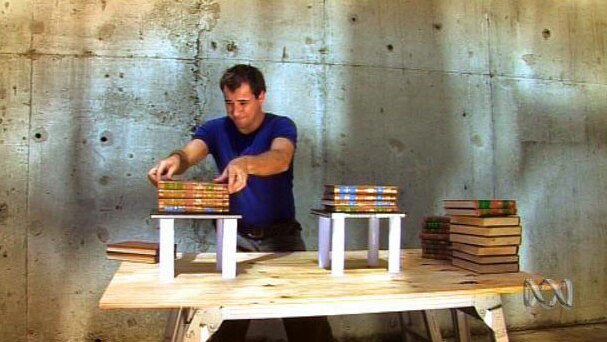 Man stacks books on top of each other on two small tables