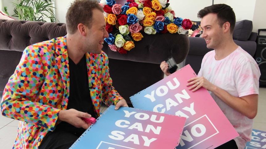 Two men hold posters that read "It's OK to say no" they will convert to wedding confetti.