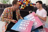 Two men hold posters that read "It's OK to say no" they will convert to wedding confetti.