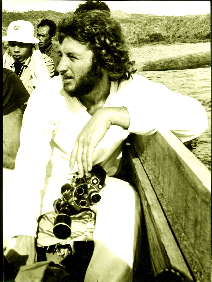 A sepia photo of a man in a boat holding an old film camera. 