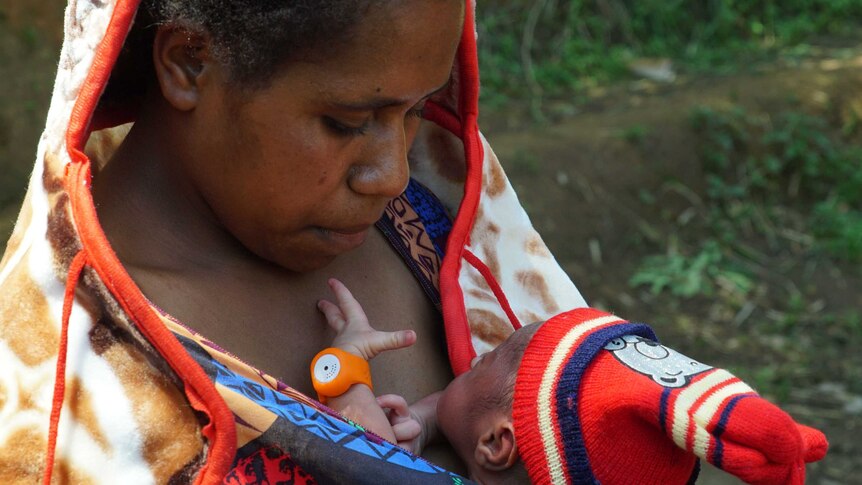 A mother cradles her baby, which is wearing a baby bracelet, close to her chest.