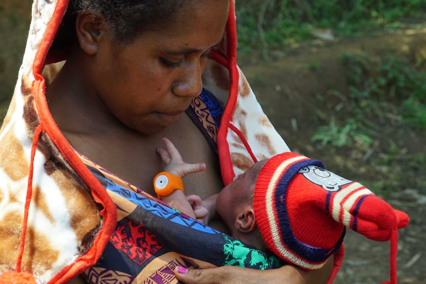 A mother cradles her baby, which is wearing a baby bracelet, close to her chest