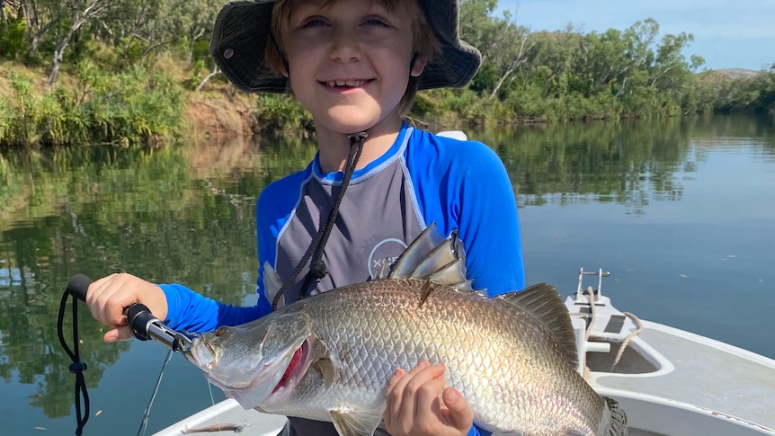 A young boy holds a large fish.